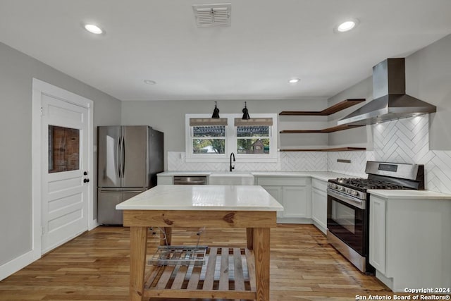 kitchen featuring wall chimney range hood, sink, light hardwood / wood-style flooring, white cabinetry, and stainless steel appliances