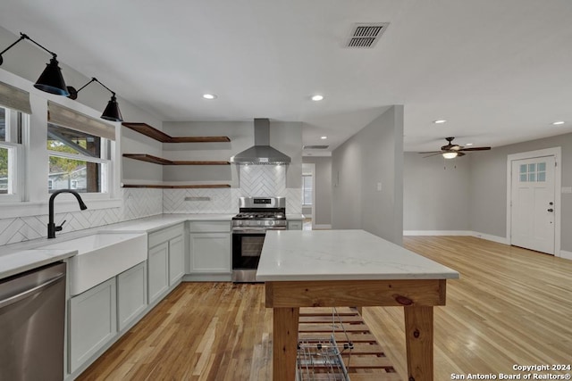 kitchen with decorative backsplash, light stone countertops, stainless steel appliances, wall chimney range hood, and light hardwood / wood-style floors