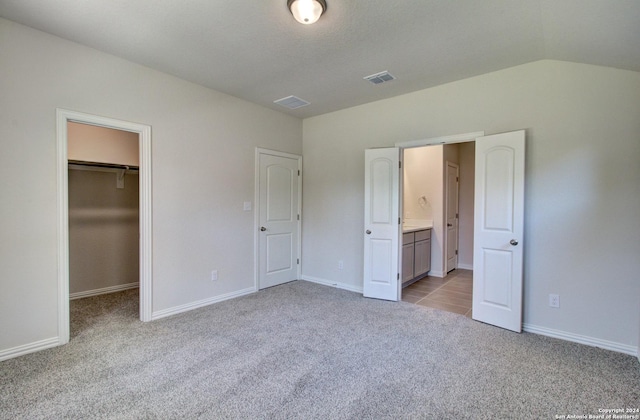 unfurnished bedroom with light carpet, a walk in closet, vaulted ceiling, and a closet