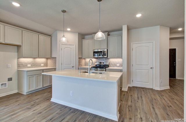 kitchen with appliances with stainless steel finishes, light wood-type flooring, tasteful backsplash, sink, and an island with sink