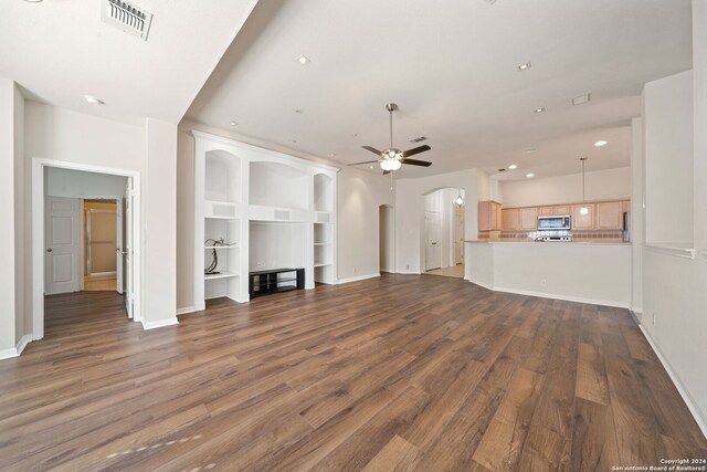 unfurnished living room featuring built in shelves, ceiling fan, and dark wood-type flooring