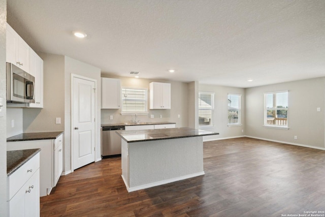 kitchen with a textured ceiling, stainless steel appliances, white cabinets, a center island, and dark hardwood / wood-style floors