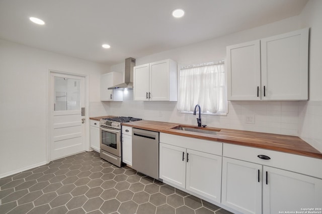 kitchen with butcher block counters, sink, wall chimney exhaust hood, white cabinets, and appliances with stainless steel finishes