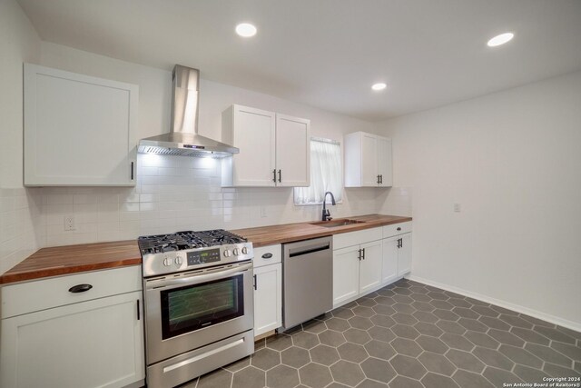 kitchen with white cabinets, butcher block counters, appliances with stainless steel finishes, and wall chimney range hood