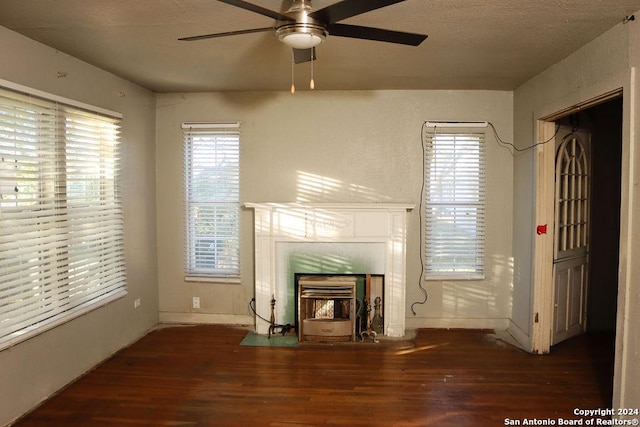 unfurnished living room featuring a tiled fireplace, ceiling fan, dark hardwood / wood-style flooring, and a textured ceiling