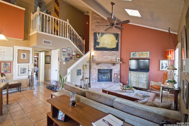 living room with high vaulted ceiling, a skylight, ceiling fan, a textured ceiling, and a fireplace