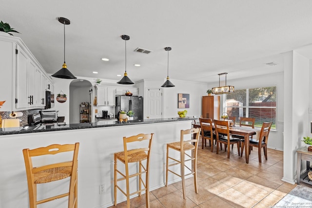 kitchen with pendant lighting, black appliances, a kitchen breakfast bar, tasteful backsplash, and white cabinetry