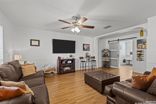 living room with ceiling fan, light hardwood / wood-style floors, and a barn door