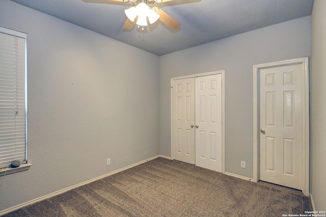 unfurnished bedroom with ceiling fan, dark carpet, and a closet