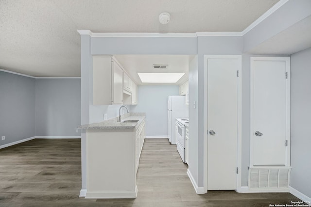 kitchen featuring white appliances, sink, hardwood / wood-style flooring, a textured ceiling, and white cabinetry