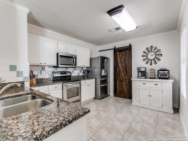 kitchen with sink, a barn door, ornamental molding, appliances with stainless steel finishes, and white cabinetry