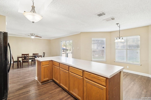 kitchen with black refrigerator, ceiling fan with notable chandelier, a textured ceiling, dark wood-type flooring, and pendant lighting