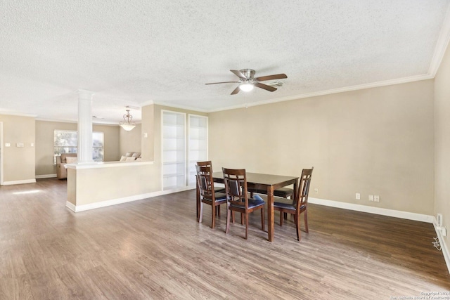 dining area with crown molding, ceiling fan, a textured ceiling, wood-type flooring, and decorative columns