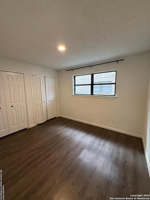 unfurnished bedroom with dark hardwood / wood-style flooring, a textured ceiling, and multiple closets