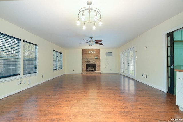 unfurnished living room featuring french doors, ceiling fan with notable chandelier, hardwood / wood-style flooring, an AC wall unit, and a fireplace