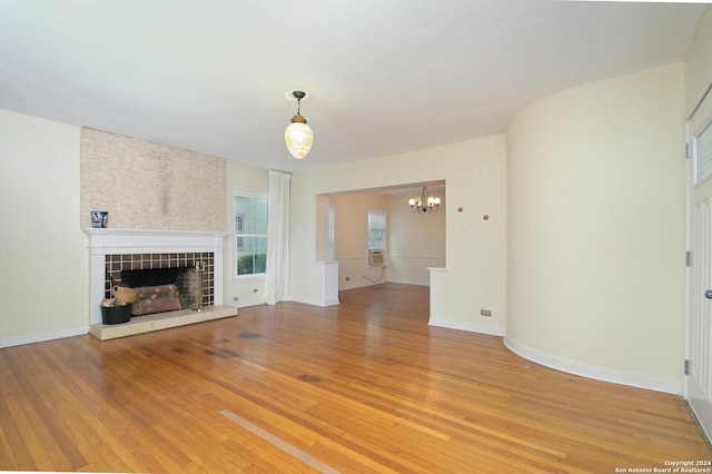 unfurnished living room featuring a tiled fireplace, a notable chandelier, and hardwood / wood-style flooring