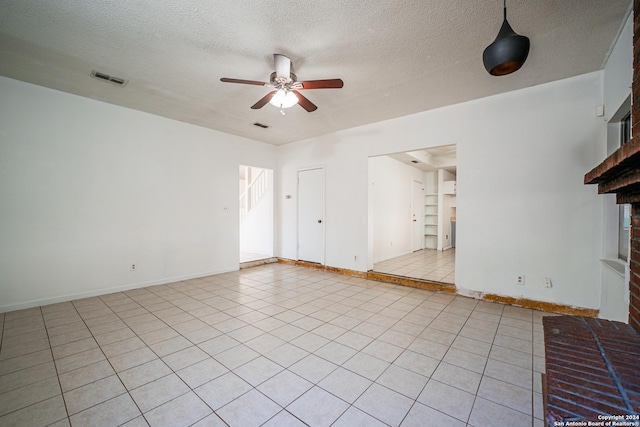 unfurnished living room with a fireplace, light tile patterned floors, a textured ceiling, and ceiling fan