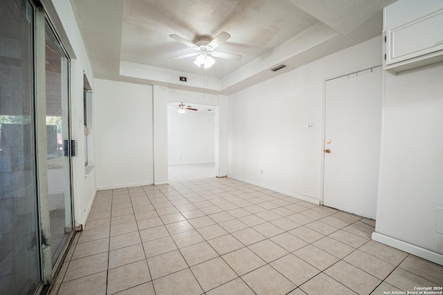 unfurnished room featuring a raised ceiling, ceiling fan, and light tile patterned flooring