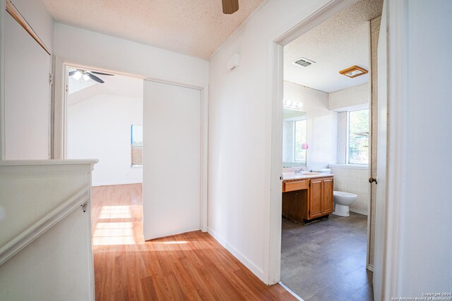 corridor with a textured ceiling, light hardwood / wood-style flooring, lofted ceiling, and sink