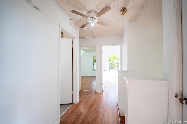 hallway featuring lofted ceiling, light hardwood / wood-style flooring, and a textured ceiling