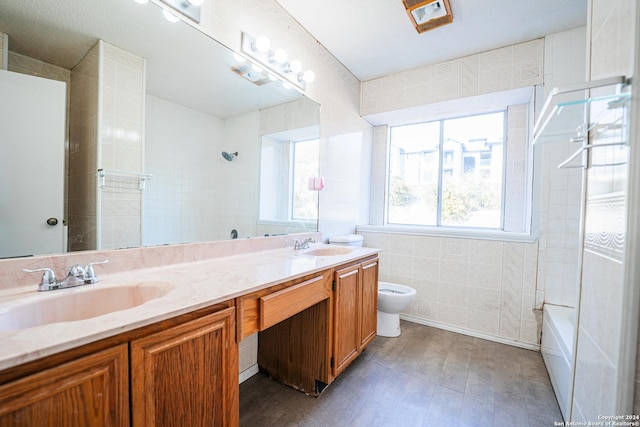 full bathroom with vanity, tiled shower / bath combo, tile walls, and toilet