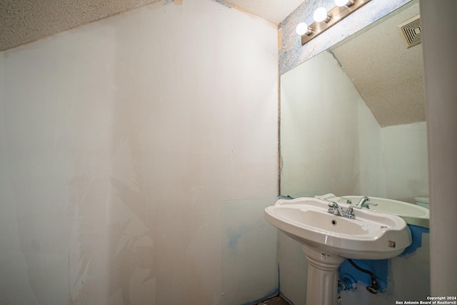 bathroom with a textured ceiling, lofted ceiling, and sink