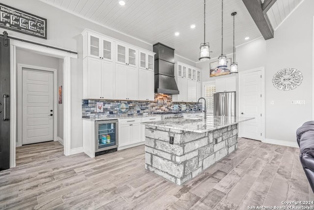 kitchen with a center island with sink, white cabinets, wall chimney range hood, wine cooler, and a barn door