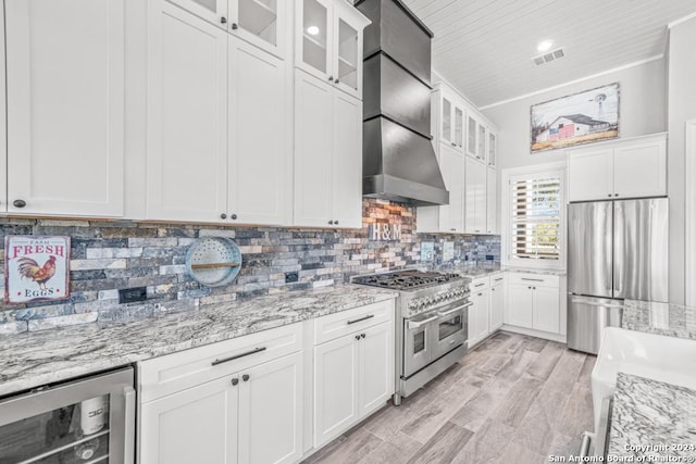 kitchen with appliances with stainless steel finishes, light stone counters, wall chimney exhaust hood, beverage cooler, and white cabinets