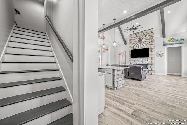 stairs featuring a fireplace, hardwood / wood-style floors, vaulted ceiling with beams, and ceiling fan