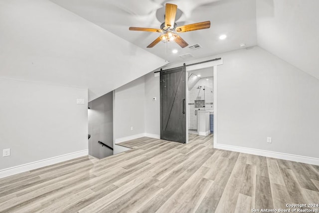 additional living space featuring lofted ceiling, a barn door, light hardwood / wood-style floors, and ceiling fan