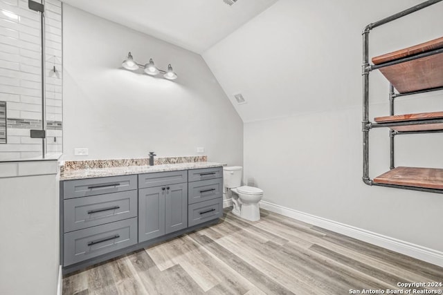 bathroom with vanity, a shower, lofted ceiling, hardwood / wood-style flooring, and toilet