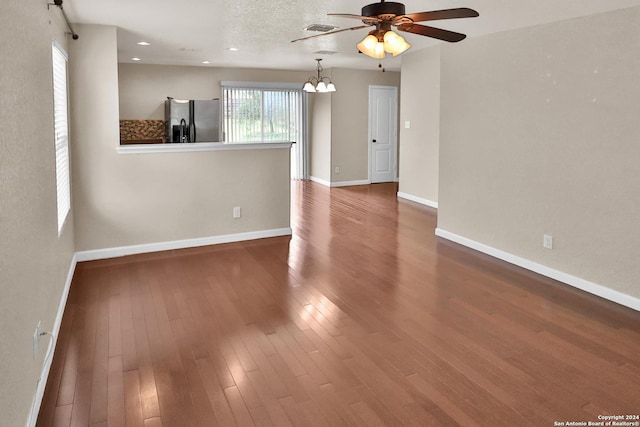 spare room featuring ceiling fan with notable chandelier, a textured ceiling, and dark wood-type flooring