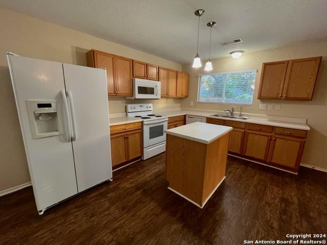 kitchen featuring a center island, white appliances, sink, decorative light fixtures, and dark hardwood / wood-style flooring