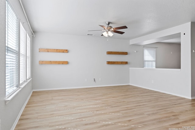 empty room with a wealth of natural light, ceiling fan, light hardwood / wood-style floors, and a textured ceiling