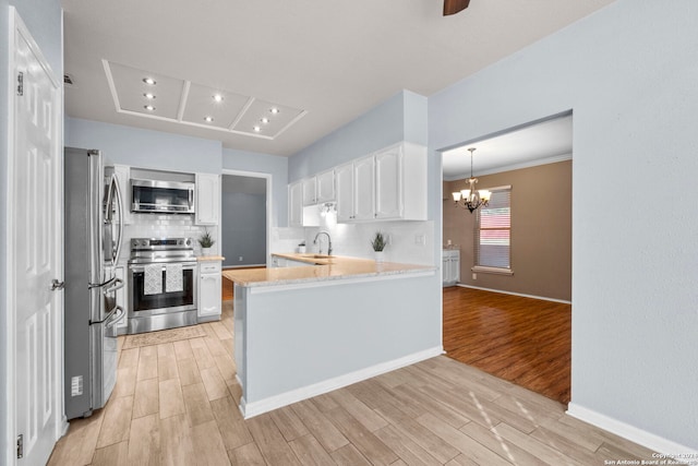 kitchen featuring kitchen peninsula, stainless steel appliances, a notable chandelier, white cabinets, and light hardwood / wood-style floors