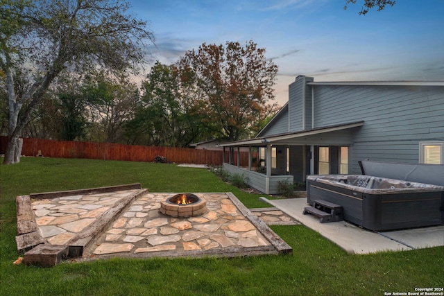 yard at dusk featuring a fire pit, a sunroom, a patio area, and a hot tub