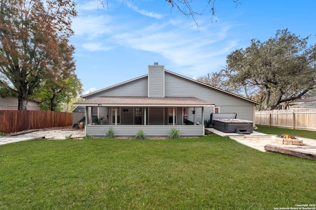 rear view of house with an outdoor fire pit, a patio area, a sunroom, a hot tub, and a lawn