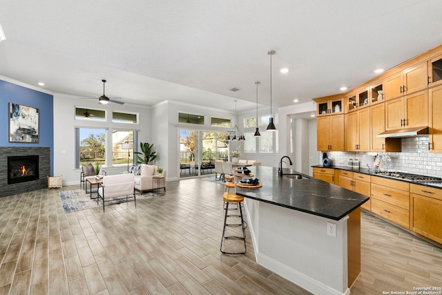 kitchen featuring a center island with sink, a stone fireplace, sink, ceiling fan, and decorative light fixtures