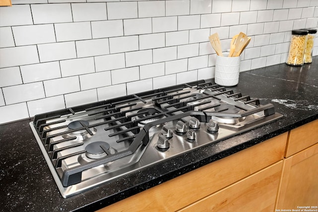 room details featuring decorative backsplash, stainless steel gas cooktop, and dark stone counters