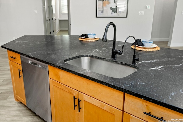 kitchen with dark stone countertops, dishwasher, light hardwood / wood-style floors, and sink