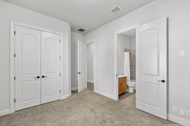 unfurnished bedroom with ensuite bathroom, light colored carpet, and a closet