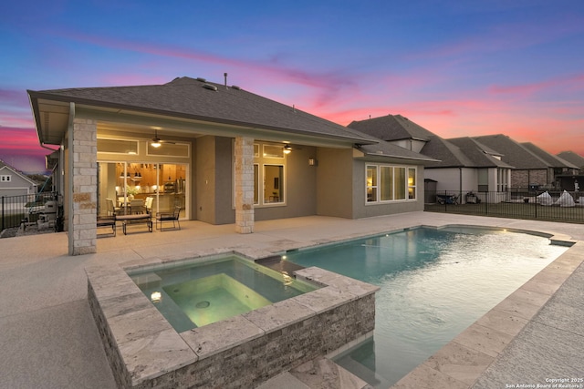 back house at dusk featuring ceiling fan, a swimming pool with hot tub, and a patio