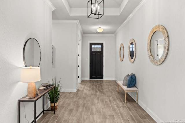 foyer entrance featuring a raised ceiling, light hardwood / wood-style flooring, an inviting chandelier, and ornamental molding