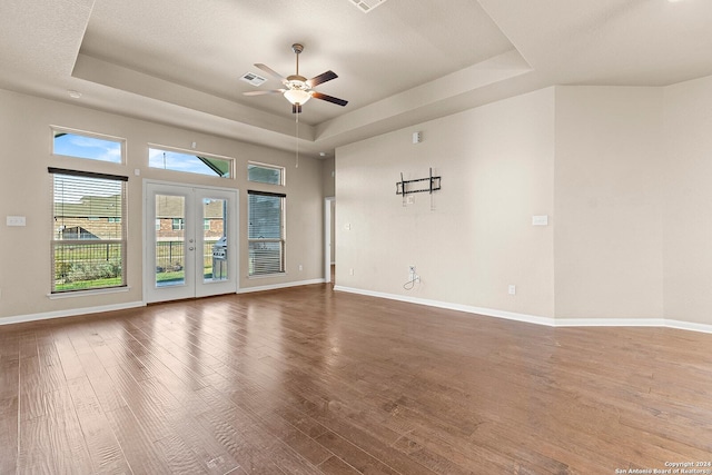 empty room featuring french doors, a textured ceiling, a tray ceiling, ceiling fan, and hardwood / wood-style floors