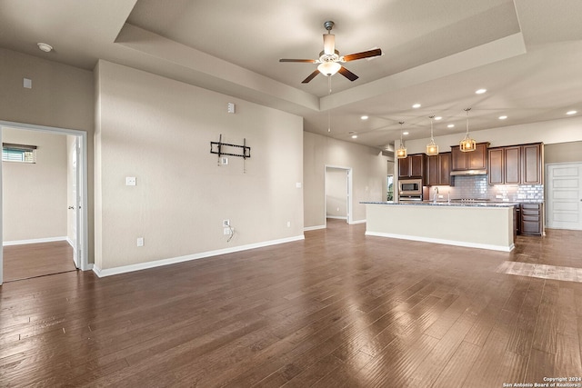 unfurnished living room with a raised ceiling, ceiling fan, dark wood-type flooring, and sink