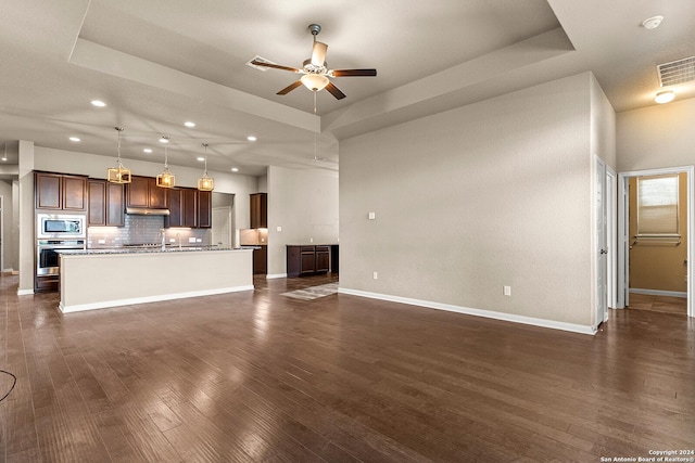 unfurnished living room featuring a tray ceiling, ceiling fan, sink, and dark wood-type flooring