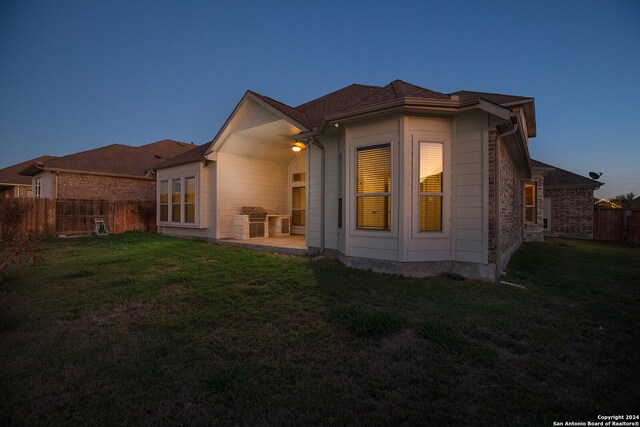 back house at dusk with a lawn and a patio area