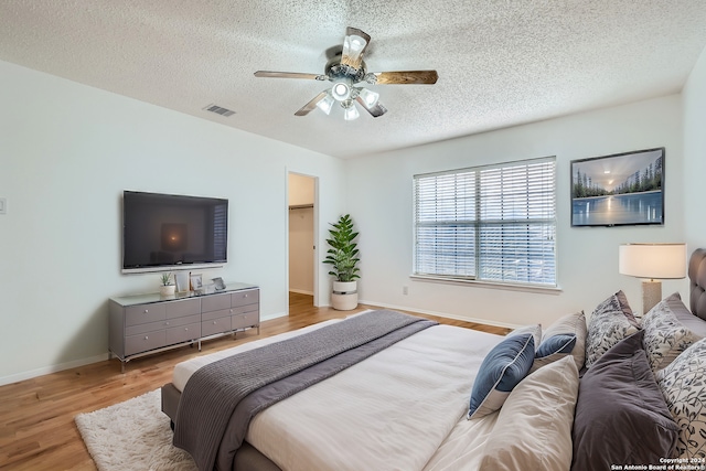 bedroom featuring hardwood / wood-style flooring, ceiling fan, a walk in closet, and a textured ceiling