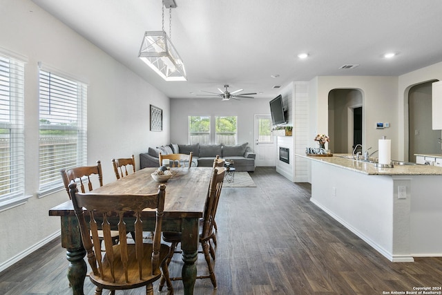 dining room with ceiling fan, a large fireplace, dark hardwood / wood-style floors, and sink