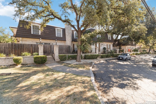 multi unit property with a fenced front yard, mansard roof, and brick siding